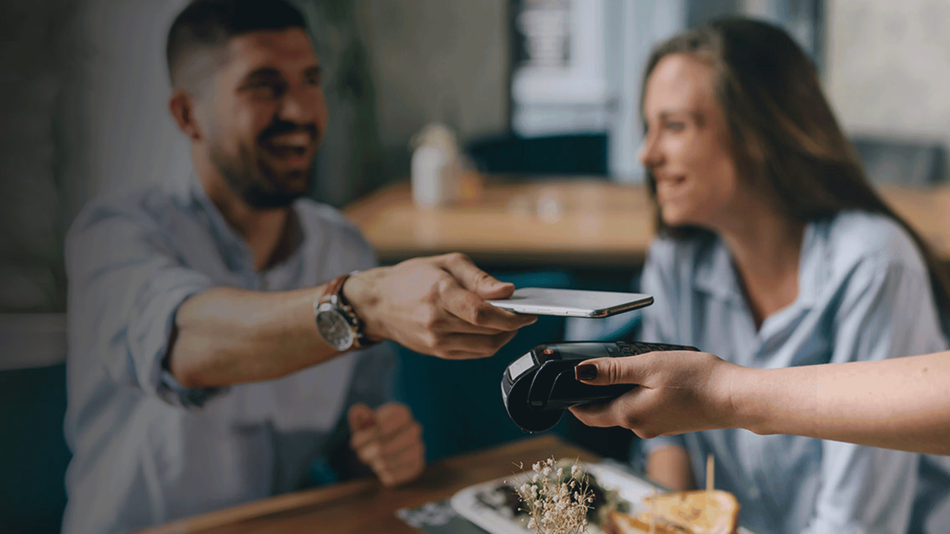Hombre pagando comida con el teléfono móvil sentado junto a una mujer.