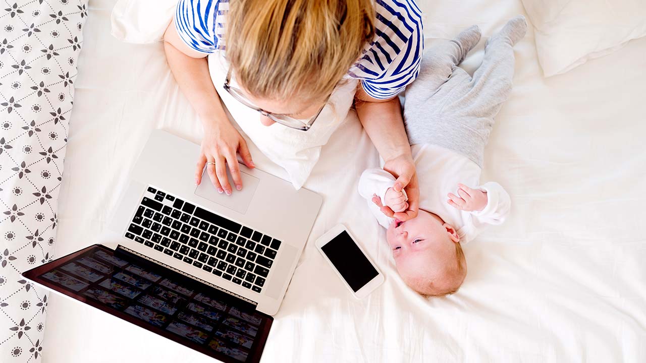 Madre con bebé junto a una computadora portátil y un teléfono móvil.