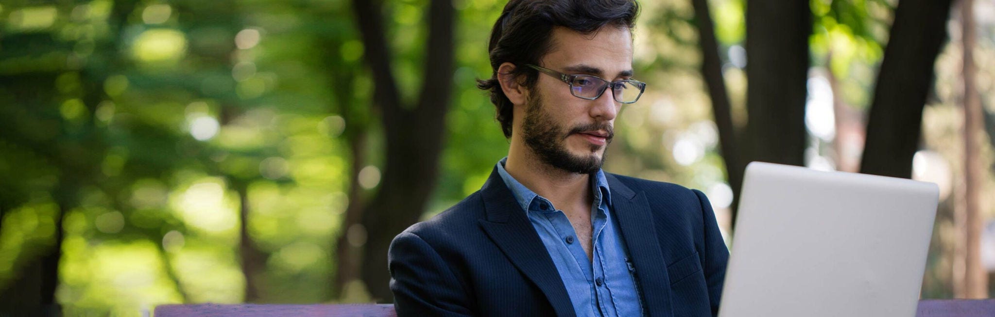 Homme en costume d'affaires dans un parc, regardant un ordinateur portable
