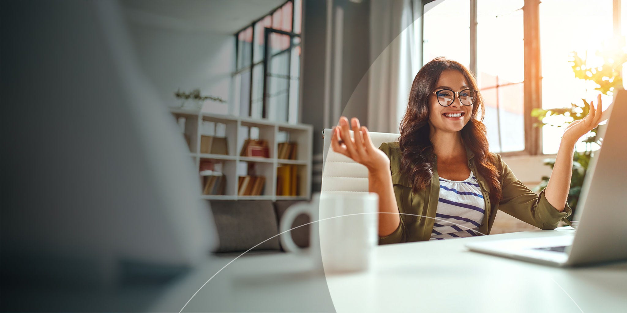 Une femme assise à un bureau, les mains levées, regardant son ordinateur portable, exprimant de l'excitation ou de la surprise.
