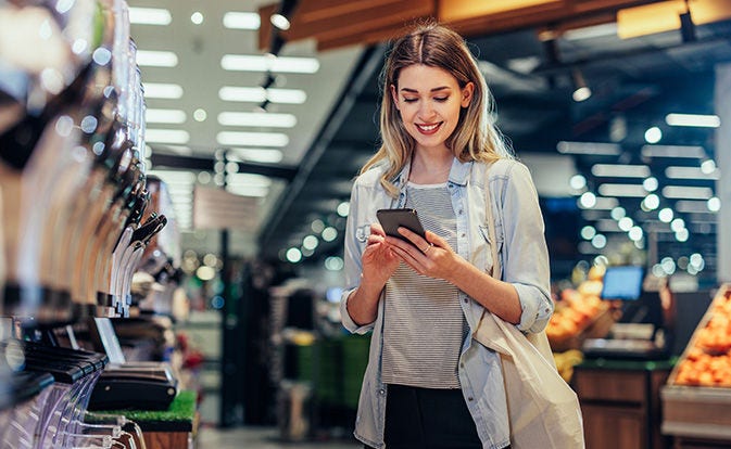 Femme souriant en utilisant son smartphone dans un espace public.
