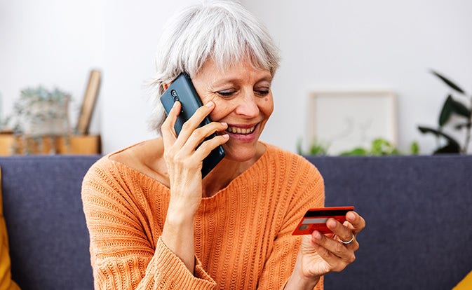 Mujer mayor comprando con tarjeta de crédito y hablando por teléfono.