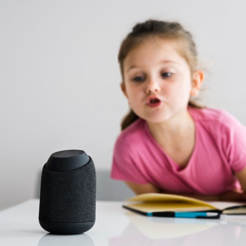 A young girl talks to a smart speaker.