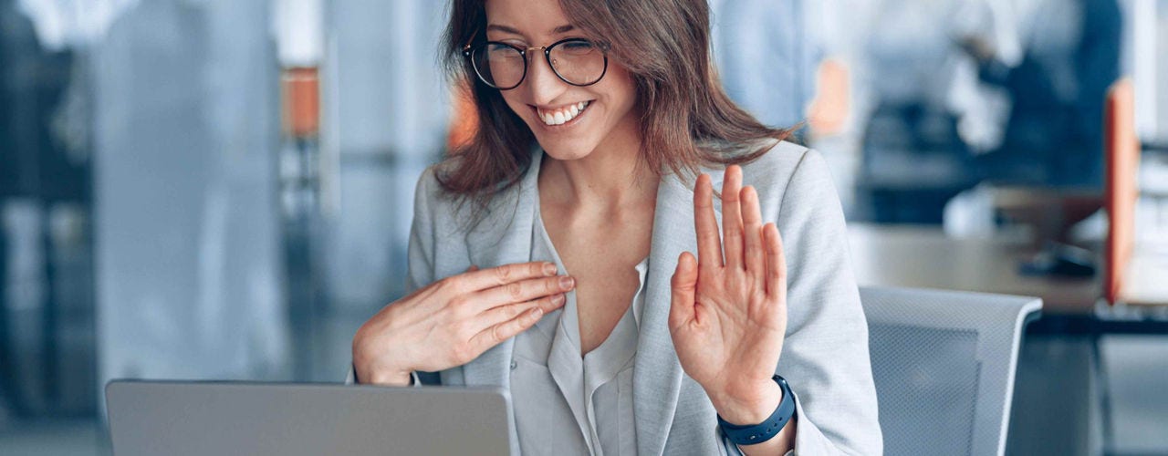 Una mujer usa el lenguaje de señas mientras se comunica con alguien a través de una computadora en una oficina. 