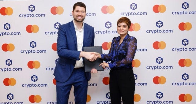 A woman lying on a couch, holding a crypto card in one hand and using the other hand to interact with a tablet device.