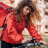Mujer compañera de reparto montando bicicleta mirando el teléfono.