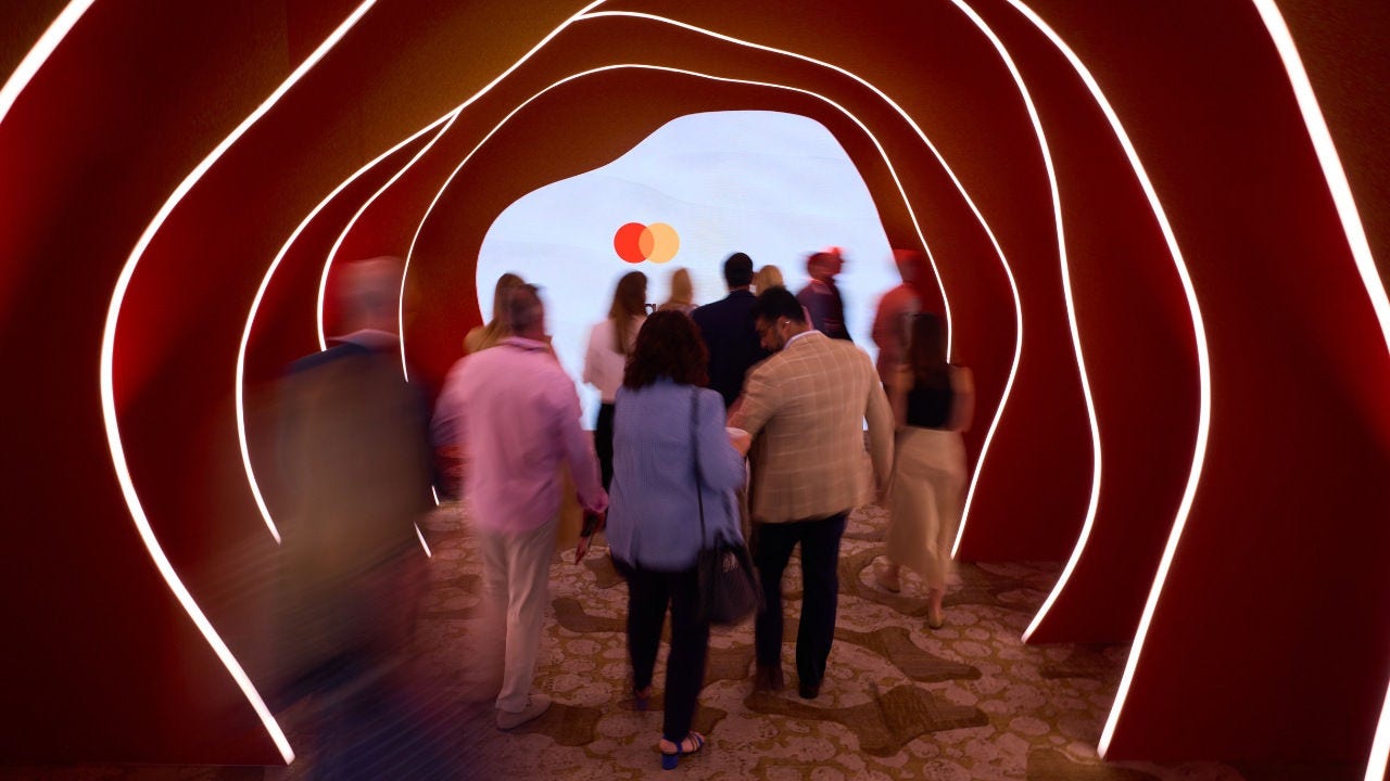 People walk through a tunnel toward a screen with Mastercard's logo on it at Connections. 
