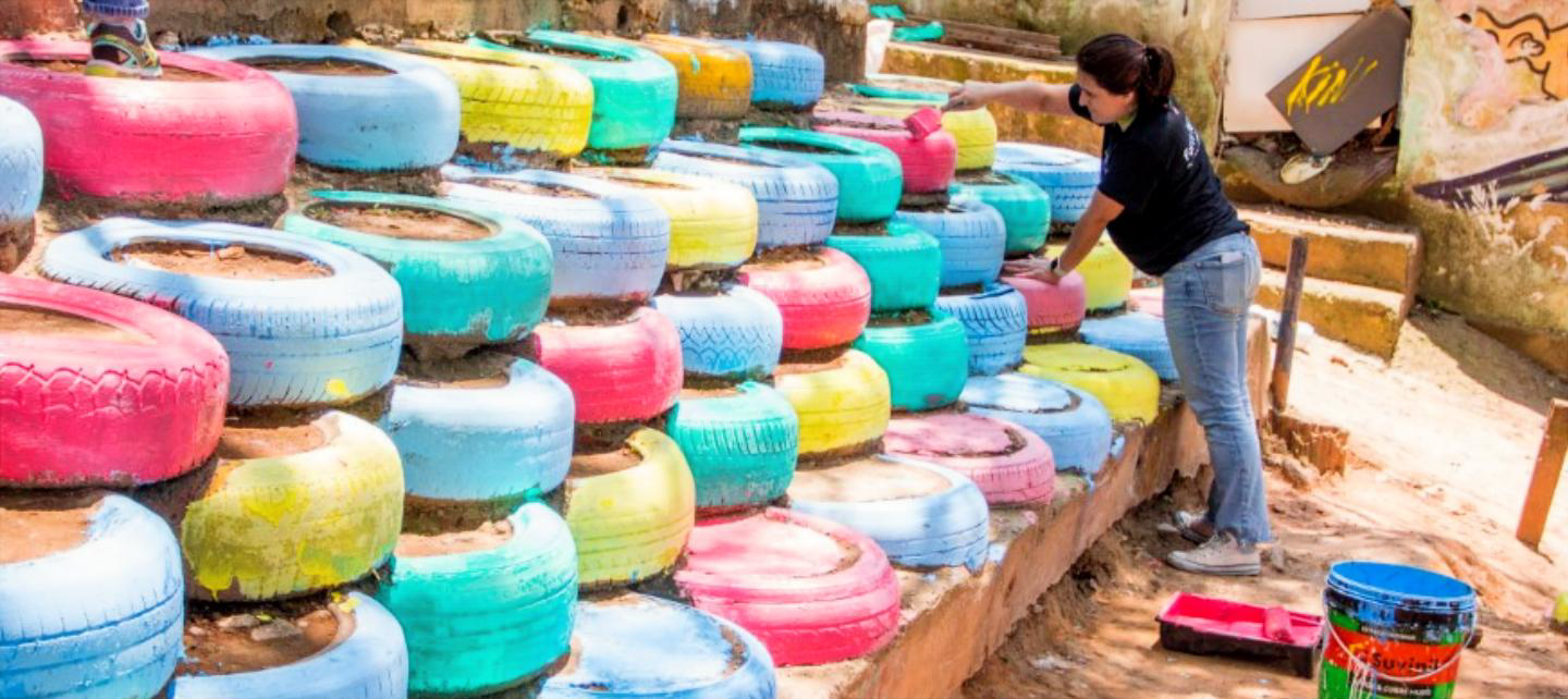 Rita Krejici paints tires stacked as a retaining wall . 