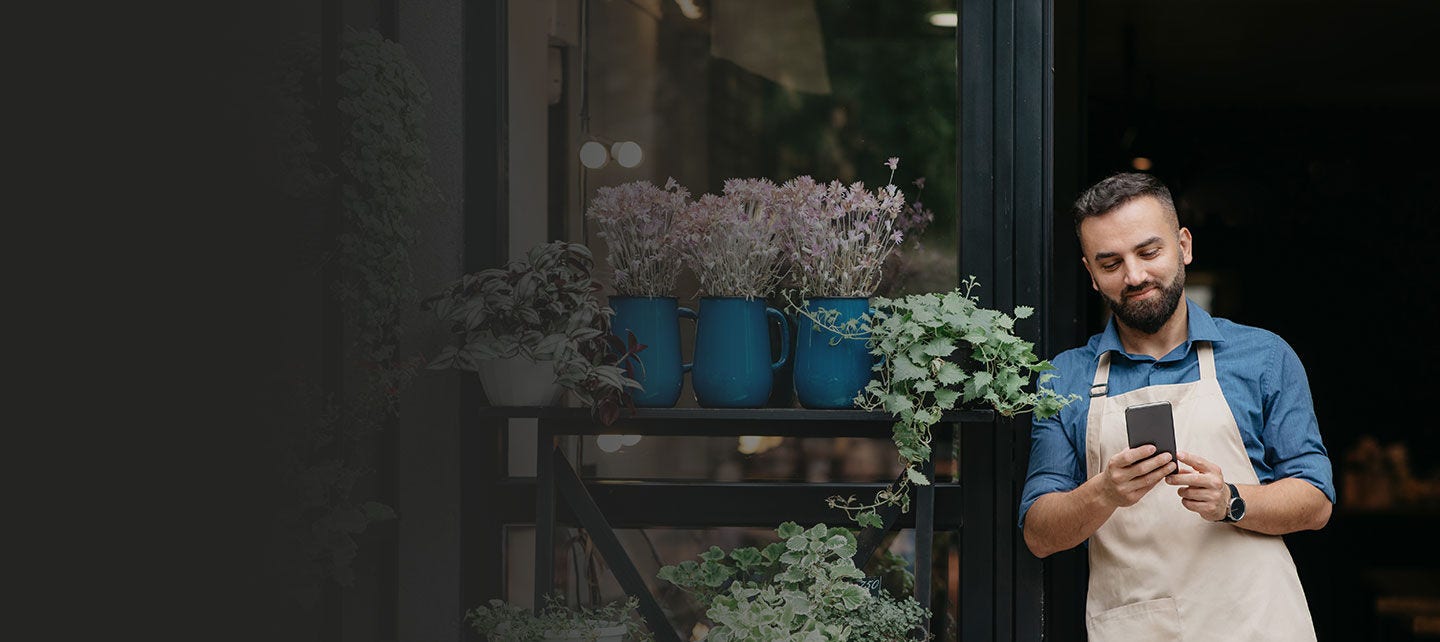 Propriétaire d’une boutique de fleurs debout devant son magasin, un téléphone à la main.