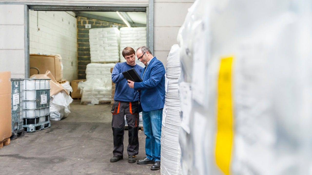 Two men standing outside a factory look at a tablet. 