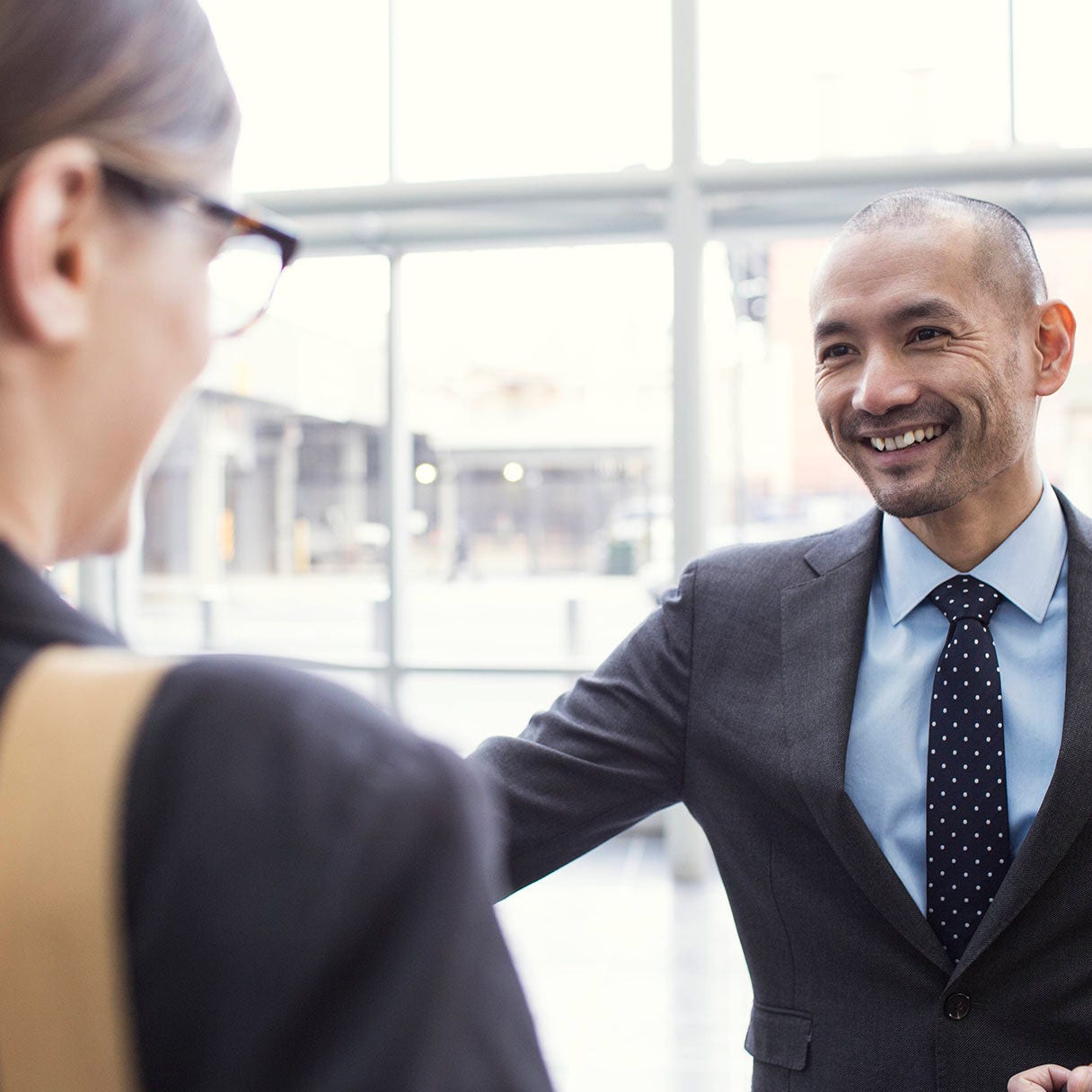 Man in a suit greeting someone in a lobby.