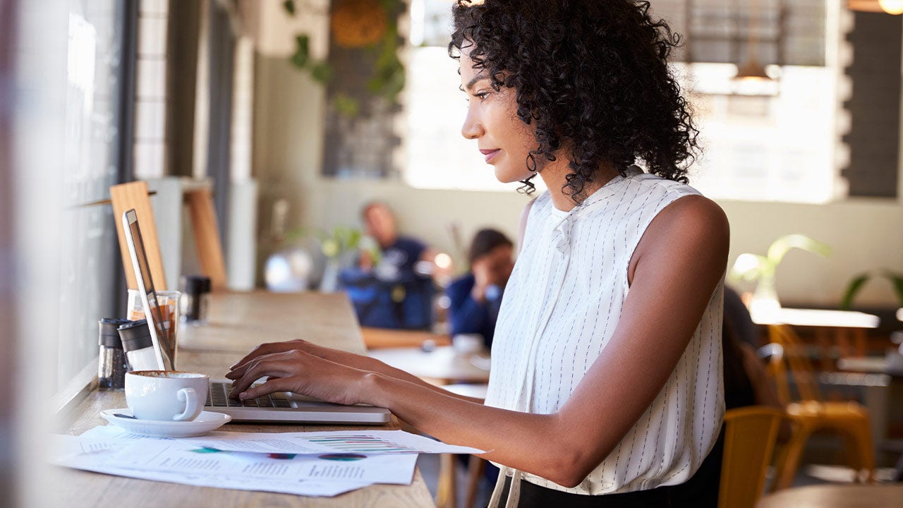 Businesswoman working on laptop by a window in coffee shop.