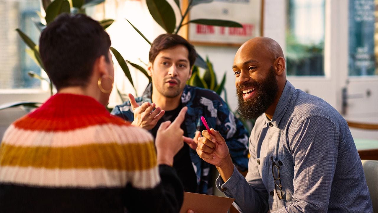 Three men engaged in conversation while seated at a table, sharing ideas and discussing various topics