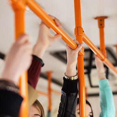 Las manos de los pasajeros agarradas a las barras de estabilidad dentro de un colectivo.