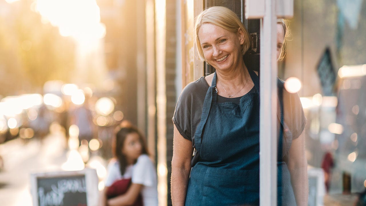 Propriétaire féminine confiante debout à l’entrée d’une épicerie fine.