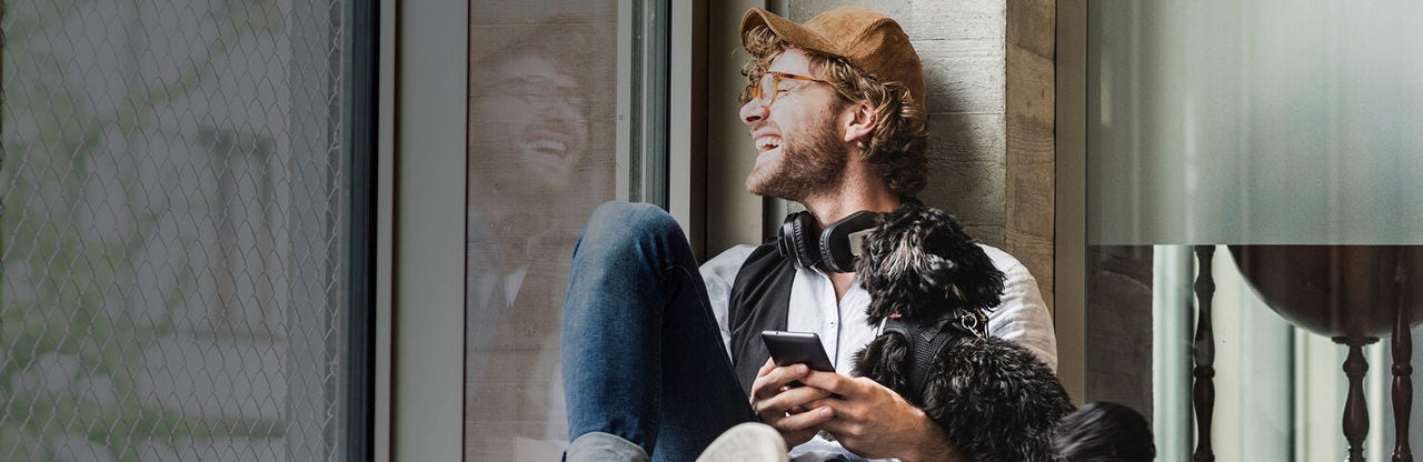 Homme souriant assis près d'une fenêtre avec un téléphone dans les mains
