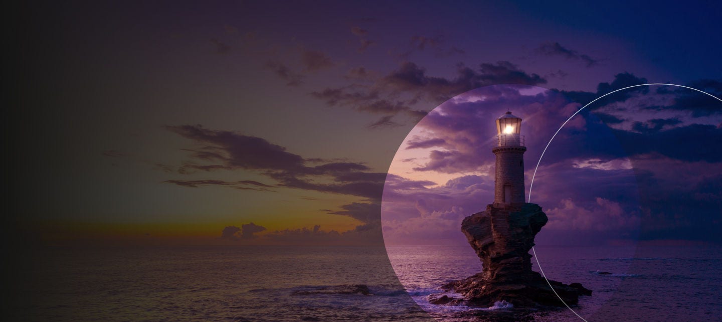 A lighthouse with a glowing light against a dramatic sunset sky.