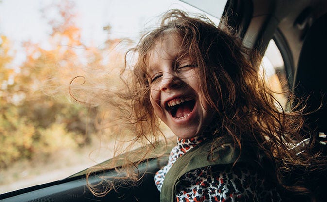 Niño sentado en un automóvil con las ventanas abiertas y el cabello ondeando al viento.