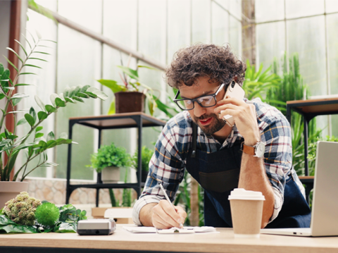 Un propriétaire de petite entreprise de sexe masculin dans une boutique de plantes, parlant au téléphone et prenant des notes, représentant la longévité des entreprises américaines.