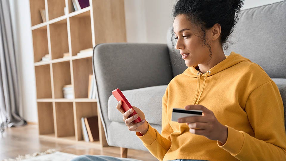 Woman making an online purchase with her phone and credit card in hand.