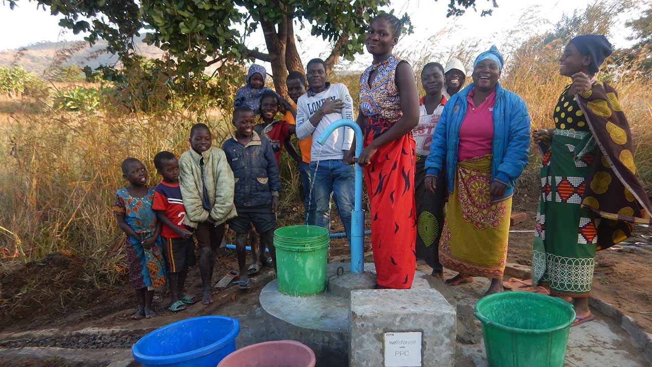 Des gens souriants devant une pompe à eau.