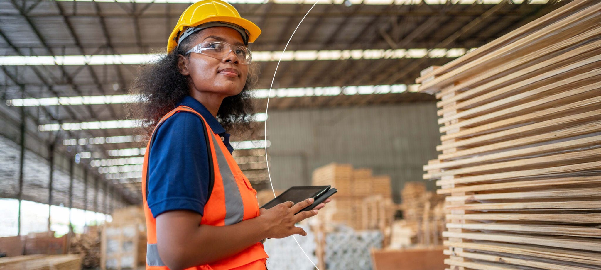 Woman in a factory with her mobile device looking into the distance
