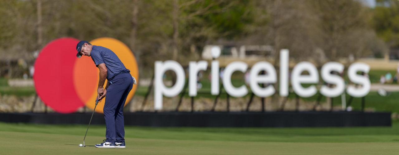 Justin Rose alinea un tiro en el green frente a un logotipo de Mastercard y un letrero de Priceless. 