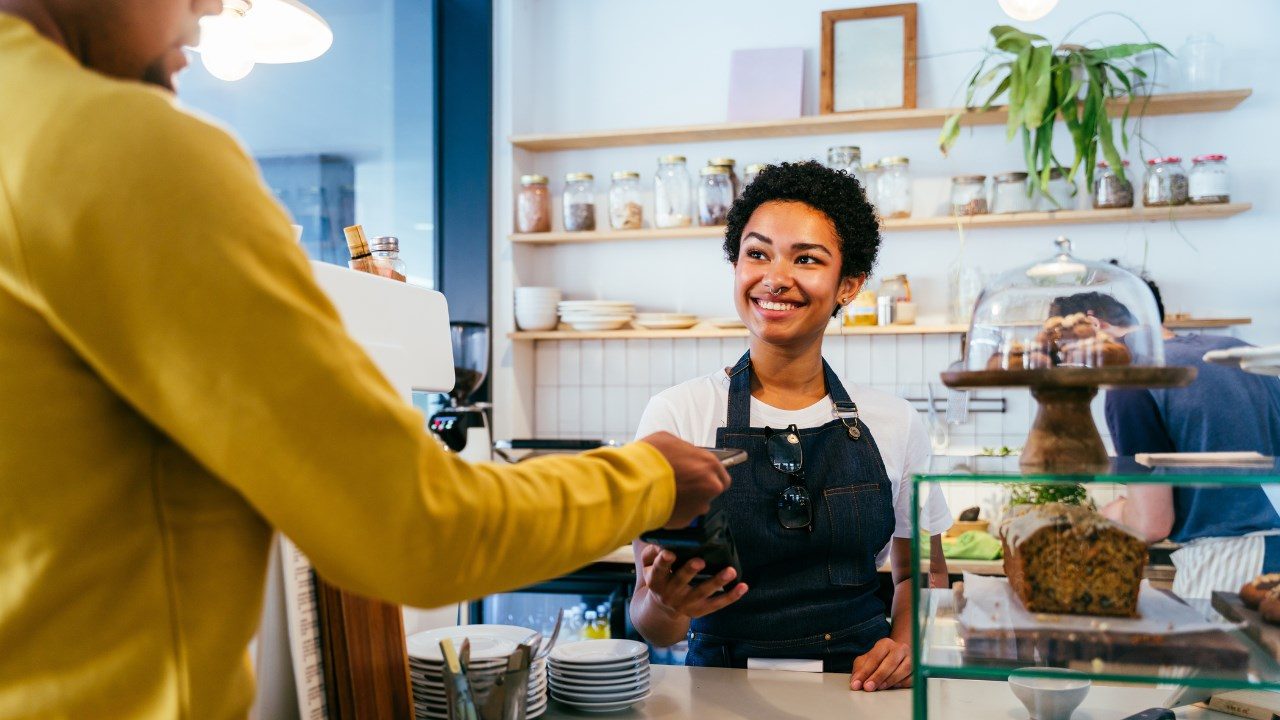 A cashier in an apron takes a digital payment from a customer. 